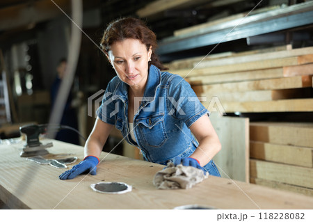During manufacturing, woman employee grinds surface of wooden board, gives smoothness to surface During manufacturing, woman employee grinds surface of wooden board, gives smoothness to surface 118228082