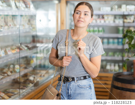 Positive young girl purchaser looking around standing next to the glass showcases in supermarket 118228123