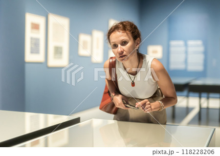 Young woman enjoying expositions in museum and looking at showcases with art objects Young woman enjoying expositions in museum and looking at showcases with art objects 118228206