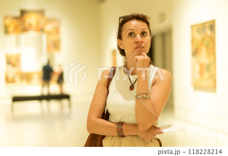 Interested woman in casual clothes exploring paintings in halls of museum 118228214