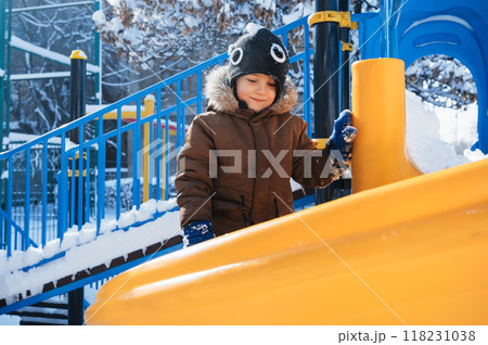 happy child boy is playing on a playground on a slide outside in winter happy child boy is playing on a playground on a slide outside in winter 118231038