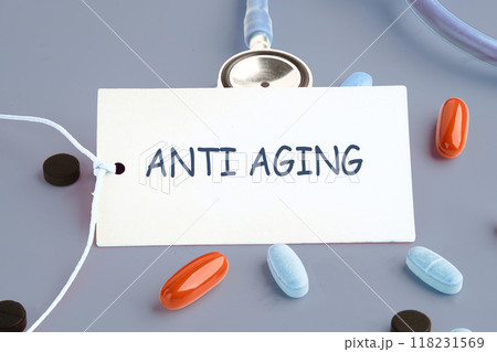 Words ANTI AGING on a white business card on a gray background next to the pills Words ANTI AGING on a white business card on a gray background next to the pills 118231569