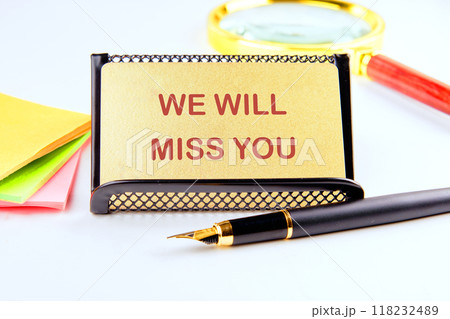 WE WILL MISS YOU written on a gold card on a stand with business accessories on a white background WE WILL MISS YOU written on a gold card on a stand with business accessories on a white background 118232489