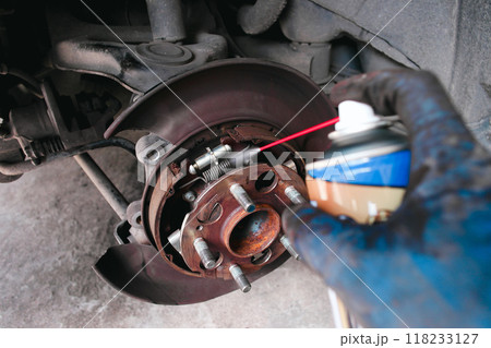 A mechanic cleans a dust the inside of a car brake drum with cleaning spray 118233127