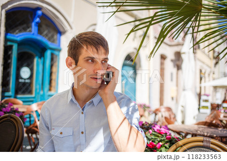 Young man on phone in a charming outdoor cafe with flowers in the afternoon 118233563