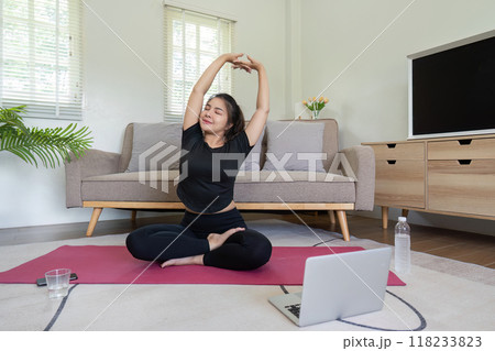 Woman practicing yoga and stretching at home with laptop 118233823