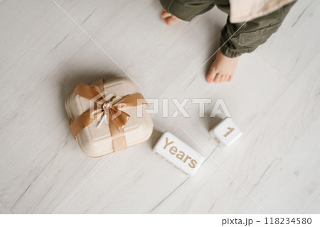 Bento cake in box tied with ribbon and candle, wooden cubes with the inscription one year old lie on the floor near the baby feet 118234580