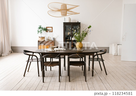 Large oval table with wooden chairs and vase of flowers in the center. Dining room is clean and well lit, giving off warm and inviting atmosphere 118234581