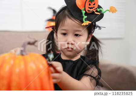 Focused Asian toddler decorating pumpkins for Halloween Focused Asian toddler decorating pumpkins for Halloween 118235825