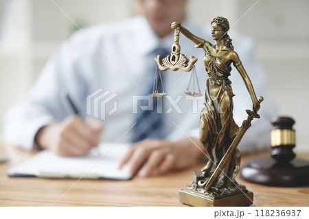 A lawyer in a suit is sitting at his desk, signing legal documents with a gavel on the side. A lawyer in a suit is sitting at his desk, signing legal documents with a gavel on the side. 118236937