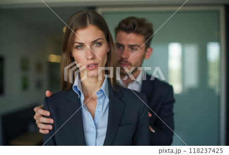 Harassment in corporate setting, male boss places hand on young female employee shoulder. Woman in formal attire visibly uncomfortable, unwanted physical contact 118237425