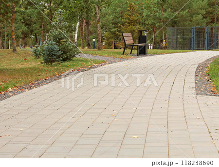 Park with coniferous trees and bench in a fashionable residential complex in summer. Nature and rest in city. Tile path. Background for design with copy space. Park with coniferous trees and bench in a fashionable residential complex in summer. Nature and rest in city. Tile path. Background for design with copy space. 118238690