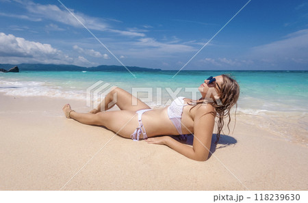 A woman relaxes on a sandy beach under a clear blue sky while enjoying the sun and ocean waves during a summer day 118239630