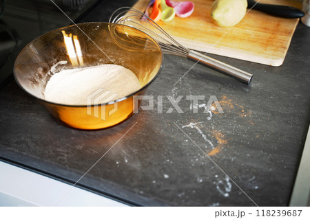 On the kitchen counter, a bowl filled with flour sits prominently beside a whisk, ready for various baking and cooking tasks On the kitchen counter, a bowl filled with flour sits prominently beside a whisk, ready for various baking and cooking tasks 118239687