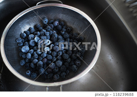 A large strainer filled to the brim with fresh blueberries sits in a clean, shiny sink, ready for washing and preparation 118239688