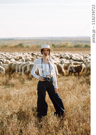 Young woman with a camera in front of a herd of sheep. Nature, fashion, vacation and lifestyle. 118239722