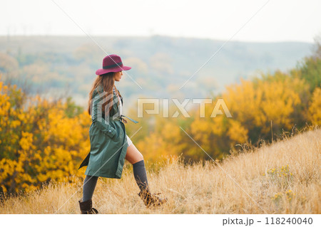 Beautiful stylish girl walks in the autumn park. The girl is dressed in a green coat and a red hat. 118240040