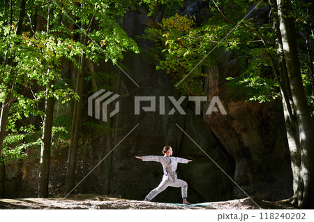 Woman practicing yoga outdoors in forest. Barefoot female on yoga mat surrounded by trees and large rocks, which suggests peaceful, natural environment ideal for meditation or yoga practice. Woman practicing yoga outdoors in forest. Barefoot female on yoga mat surrounded by trees and large rocks, which suggests peaceful, natural environment ideal for meditation or yoga practice. 118240202