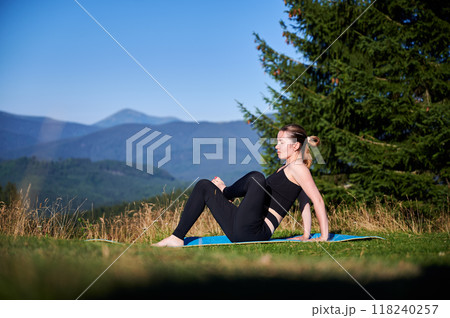 Woman practicing yoga outdoors in the mountains in a serene, natural setting. Female performing yoga pose on mat, with backdrop of beautiful mountain landscape at sunrise or sunset. Woman practicing yoga outdoors in the mountains in a serene, natural setting. Female performing yoga pose on mat, with backdrop of beautiful mountain landscape at sunrise or sunset. 118240257