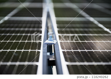 Close up of mounting hardware on solar panel, focusing on the details of the securing mechanism. Bolt and mounting structure against the blurred lines of photovoltaic cells stretching into background. Close up of mounting hardware on solar panel, focusing on the details of the securing mechanism. Bolt and mounting structure against the blurred lines of photovoltaic cells stretching into background. 118240262