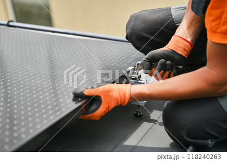 Worker building photovoltaic solar panel system on rooftop of house. Close up of man engineer in gloves installing solar module with help of hex key outdoors. Renewable energy generation concept. Worker building photovoltaic solar panel system on rooftop of house. Close up of man engineer in gloves installing solar module with help of hex key outdoors. Renewable energy generation concept. 118240263