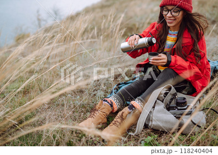 Beautiful woman drinking tea from thermos on cold autumn day. Rest, relaxation, lifestyle concept. Beautiful woman drinking tea from thermos on cold autumn day. Rest, relaxation, lifestyle concept. 118240404