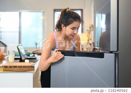 Smiling young woman looking inside the fridge, searching for ingredients while preparing a meal or snack Smiling young woman looking inside the fridge, searching for ingredients while preparing a meal or snack 118240562