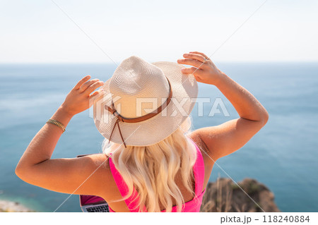A woman wearing a white hat and a pink tank top is standing on a beach with her hands in the air. She is looking out at the ocean and has a laptop in her hand. Concept of relaxation and leisure. A woman wearing a white hat and a pink tank top is standing on a beach with her hands in the air. She is looking out at the ocean and has a laptop in her hand. Concept of relaxation and leisure. 118240884