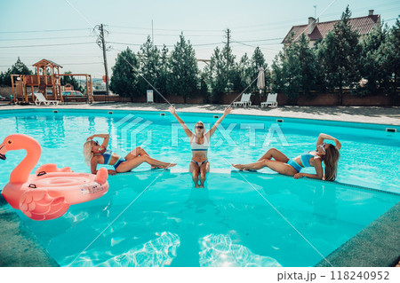 Three women are sitting in a pool, one of them is wearing a pink floatie. Scene is lighthearted and fun, as the women are enjoying their time together in the pool. 118240952
