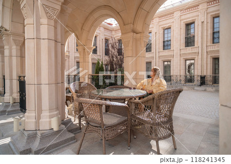 Man, Patio, Building - A lone man sits at a table on a patio in front of a building. 118241345