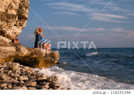 Woman Cliff Ocean - Young woman in denim jacket sits on a cliff overlooking the ocean. 118241346