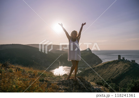woman standing hill with her arms raised in the air, looking up at the sun. The scene is peaceful and serene, with the woman's expression conveying a sense of joy and happiness. 118241361