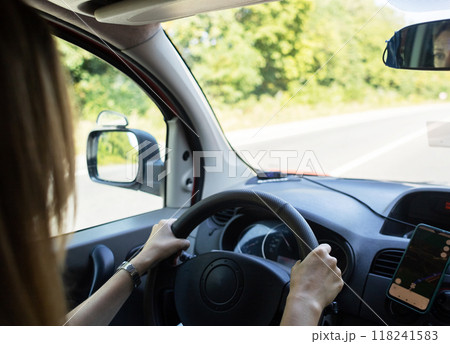A woman drives a car and looks intently at the track. The navigator on the smartphone shows the map and the correct direction. Driving lessons on a manual transmission A woman drives a car and looks intently at the track. The navigator on the smartphone shows the map and the correct direction. Driving lessons on a manual transmission 118241583