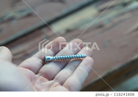 The white man's left hand holds in palm of his hand furniture fastener called European-type screw, Euroscrew, or sometimes called a confirmation fastener. The head is screwed with a hex socket wrench. 118241606