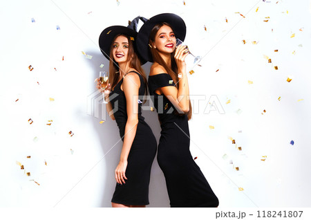 portrait of two happy young women in black witch halloween costumes on party over white background. portrait of two happy young women in black witch halloween costumes on party over white background. 118241807