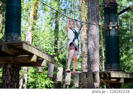 Young girl participating in outdoor adventure park, navigating through a rope obstacle course 118242228
