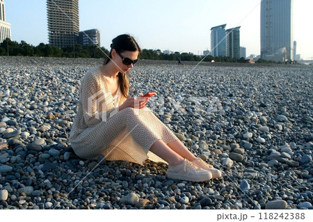 Woman browsing smartphone sitting on pebble coast in Batumi city Georgia. 118242388