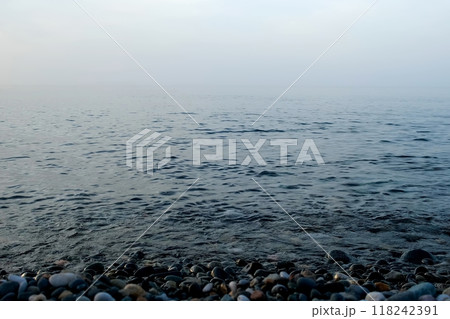 Pebble beach with small pebbles calm sea water surface and fog over sea. 118242391