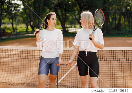 Female friends with racquets and box of balls on the tennis court. Summer, outside court. Female friends with racquets and box of balls on the tennis court. Summer, outside court. 118243653