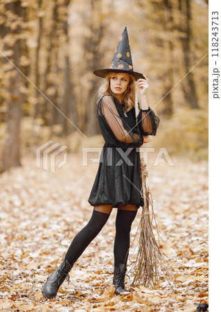 Blonde young girl witch in forest on Halloween. Girl wearing black dress and cone hat. Witch holding a broom. 118243713