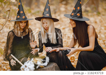 Three girls witches in forest on Halloween. Girls wearing black dresses and cone hats. Witches make a magic potion. 118243719