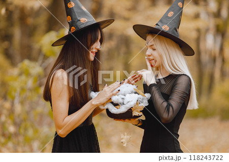 Two young girls witches in forest on Halloween. Girls wearing black dresses and cone hat. Witch holding a magician cauldron. 118243722