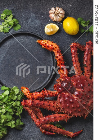 Top view of fresh king crab legs, herbs, and lemon wedges surrounding an empty black plate on a dark textured background, ready for a gourmet seafood preparation Top view of fresh king crab legs, herbs, and lemon wedges surrounding an empty black plate on a dark textured background, ready for a gourmet seafood preparation 118245022