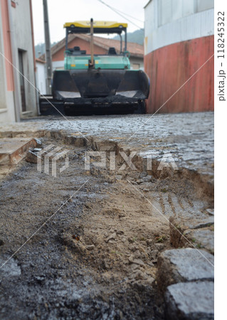 Porto, Portugal - 2024, September 1: Close-up of a hole in an old paving stone and an asphalt paver in the background. Concept of repair work in old, historical cities, urban development technologies. 118245322