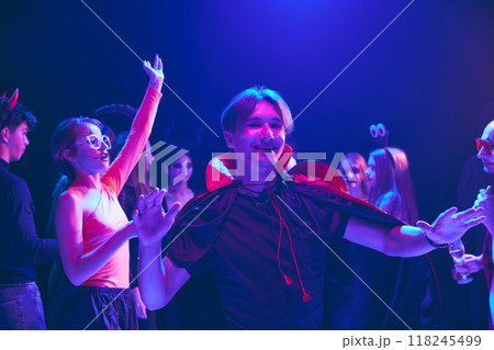 Group of young friends in Halloween costumes sharing laugh at party at nightclub, cheerfully dancing and having fun. Group of young friends in Halloween costumes sharing laugh at party at nightclub, cheerfully dancing and having fun. 118245499