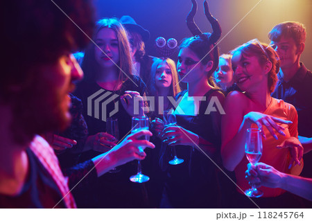 Group of young friends, dressed in spooky and fun costumes, attending nightclub for cheerful celebration of Halloween Group of young friends, dressed in spooky and fun costumes, attending nightclub for cheerful celebration of Halloween 118245764