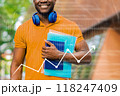 A man in an orange shirt is holding a stack of books and wearing headphones 118247409