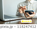 A man is using a cell phone while sitting at a desk with a laptop 118247412
