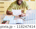 A man is sitting at a desk with a laptop and a stack of papers 118247414