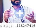 A man wearing a white lab coat is holding a stethoscope and smiling 118247416
